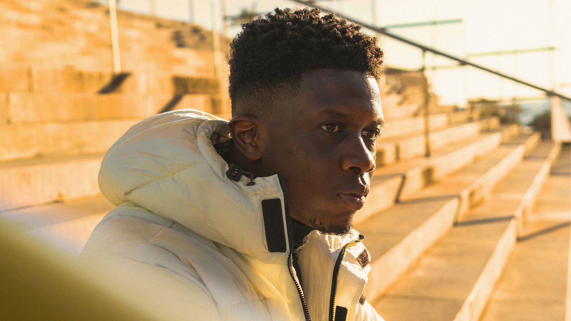 Black teen in a cream coat sitting outside on steps